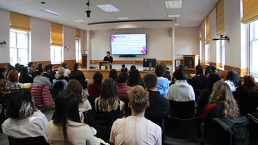 Moot court set up in a lecture style room with the presenter at the front with a presentation. Room is filled with a audience watching the lecture