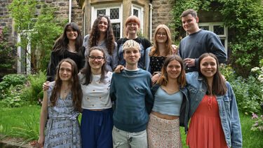 10 students in 2 row arms around each other looking at the camera in a garden