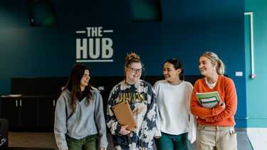 Four girls walking towards the camera, they have books in their arms and are laughing together