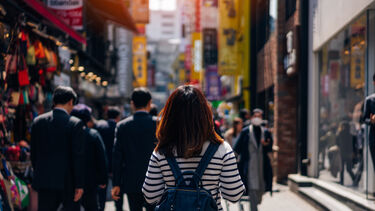 A young female tourist walking down a busy shopping street in Seoul, South Korea