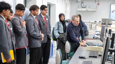 A group of five male students wearing school uniforms watch Professor Chris Stokes show them something on a computer screen.