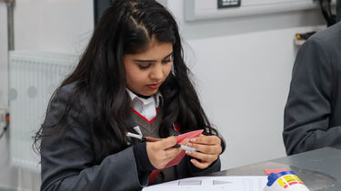 A female student wearing a school uniform pushing out a square of wax from a sheet