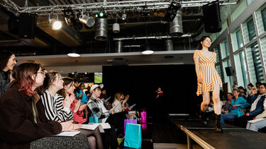 Asian girl walking down a catwalk with rows of people seated either side