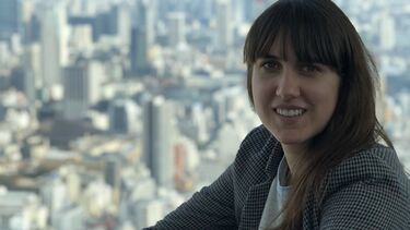 A woman sits at a window against a city backdrop