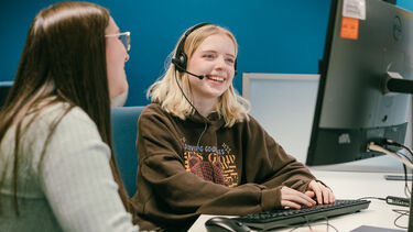 Senior student going through how to handle a call to the pro bono clinic. The new student advisor is smiling whilst responding to a call imputing information on a PC. We can only see the back of the PC