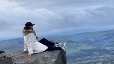 Jing sitting on the edge of a cliff overlooking a valley.
