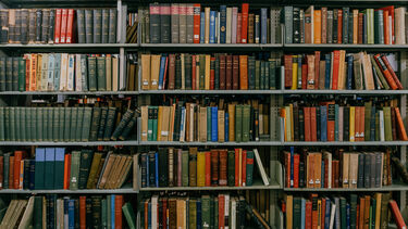 6 bookshelves in a library filled with lots of old textbooks of colours