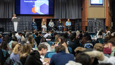 A panel of students on a stage in front of a large crowd of students.