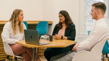 Three people sat round a table working together.