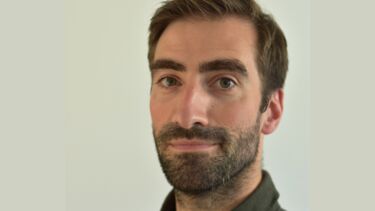 A man with dark hair wearing a brown shirt