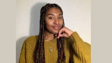 A woman with long braided hair and a yellow jumper.
