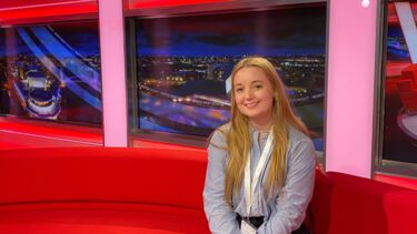 Marti Stelling, sitting on a black sofa in a TV Studio.