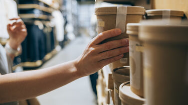 A close up of a woman holding a product in biodegradable packaging in a supermarket