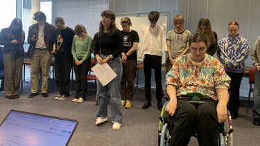 Group of people standing in a line with two students in gthe foreground, one clearly speaking