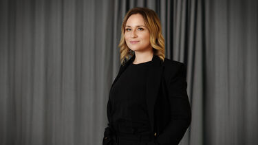 A woman with blonde hair, wearing a black jacket and blouse. 