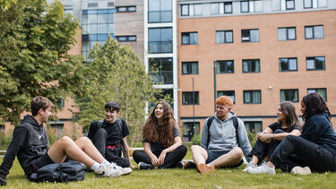A group of students sat on the grass in front of an accommodation building
