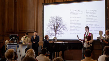 5 speakers on a stage, with one sat at a piano 