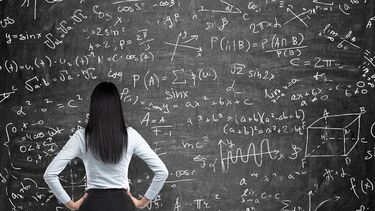 Photo of an academic looking at a blackboard covered in equations