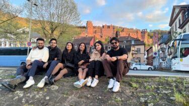 MBA students sitting on a grass bank in a town centre.