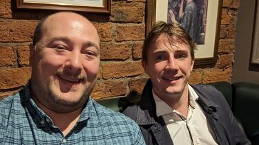 Two men sitting in venue smiling at camera 