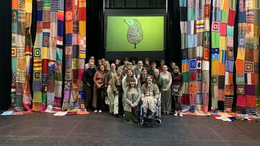 group of students in a theatre between multicoloured curtains with the drawing of a hedgehog in the background