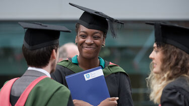 girls smiles in a graduation gown holding her graduation certificate 