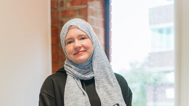 Ameena faces the camera, smiling, with her arms folded at the front. 