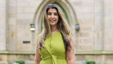 Asha stands smiling at the camera with St George's Church in the background.