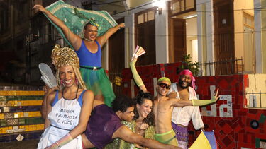 A group of peple wearing colourful clothes and headresses posing as if taking part in a carnival