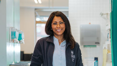Cynthia stands in her examination room with her hands in her pockets and smiles at the camera. 