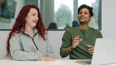 Two students - one with long red hair, one with short dark hair - laughing together.