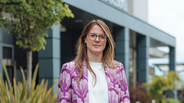 Faith stands in front of a building with plants either side of her 