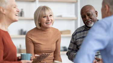Portrait of cheerful pensioners sitting in circle, drinking tea and chatting, happy multiracial senior women and men in casual enjoying time together at retirement house, having conversation