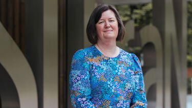 Heather stands in front of the SITraiN sign with her hands folded in front of her