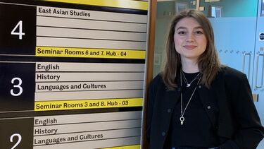 academic visitor from Ukraine Vira Dutkanych leaning against a bord indicating what is on which floor in Jessop West