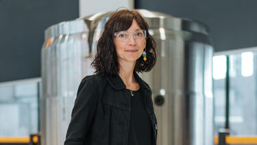 Iwona stands in front of polished cylinder with her hands in her pockets 