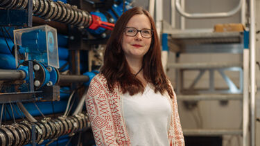 Katherine stands in front of a replica of a water pipe system.
