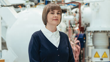 Marie stands smiling at the camera with her hands folded in front of her.