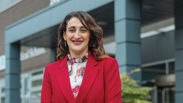 Munitta stands in front of a building with plants either side, her hands are crossed in front of her 