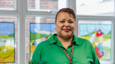 Rhonda stands hands in pockets, smiling and facing the camera. Behind her are three stained glass panels. 