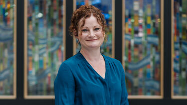 Ruth stands facing the camera with a stained glass behind her