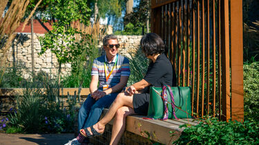 Two people sitting on a bench in a small park area talking to each other