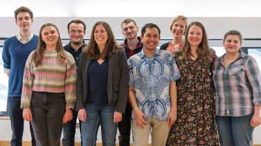Nine people stand facing and smiling at the camera 