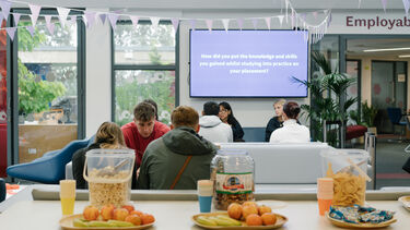 Students attending a paid work drop in session at the Management School. Students are sitting in groups discussing work opportunities, and snacks are provided on a table nearby. 