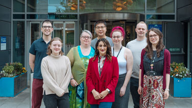 A group of 8 people stand and face the camera smiling. 