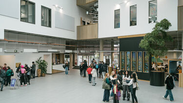 Interior shot of a large open plan building. Students walk through.