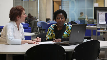Two people sit at a table looking at a laptop
