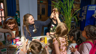 Adult female engaging group of children with plants and food items at community outreach event