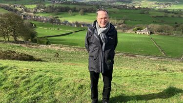 Bob stood in a field with a beautiful view of countryside behind him