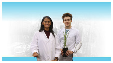 A male and a female researcher in lab coats holding a potted plant